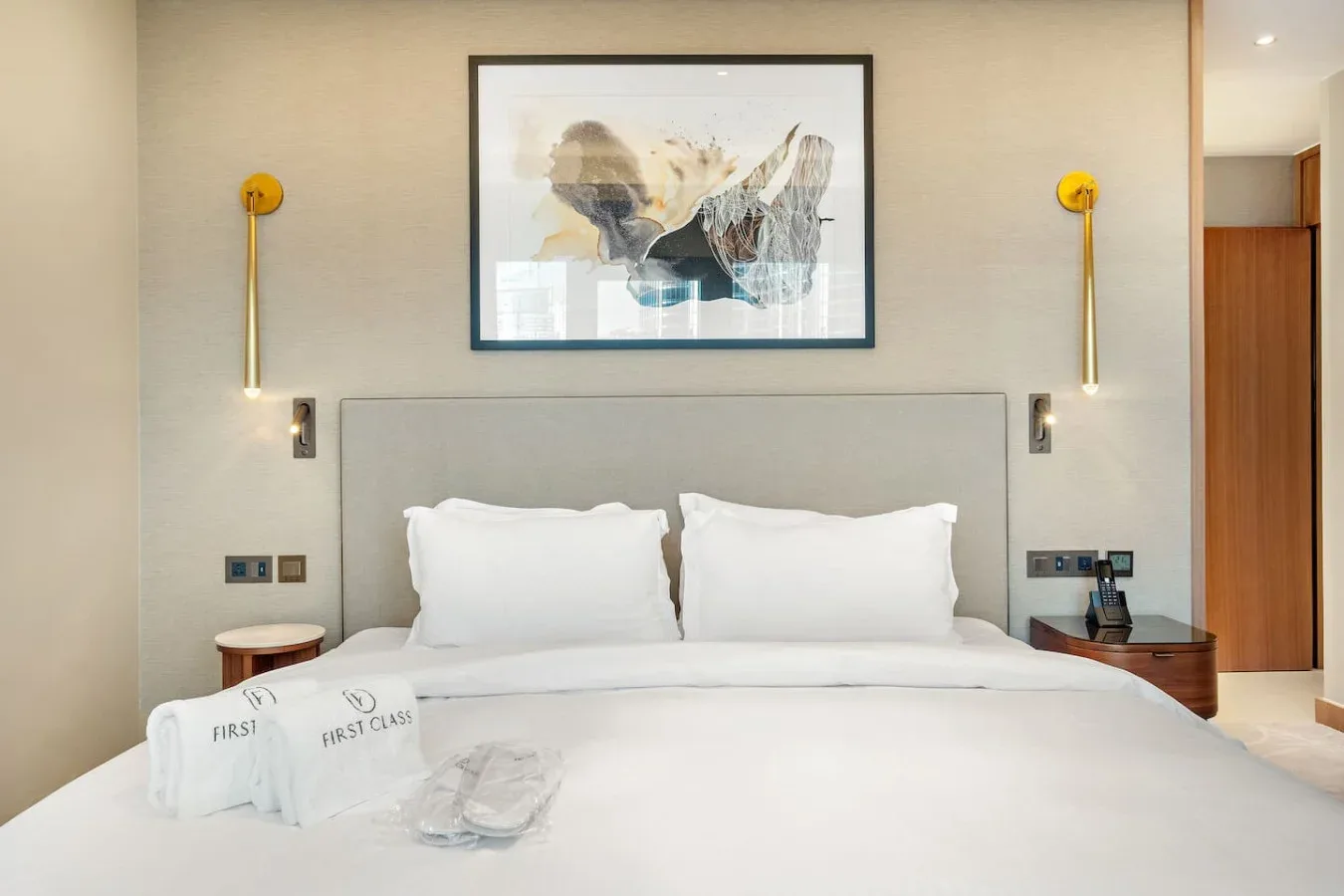 A bedroom with a neatly made bed beneath framed artwork and wall lights.