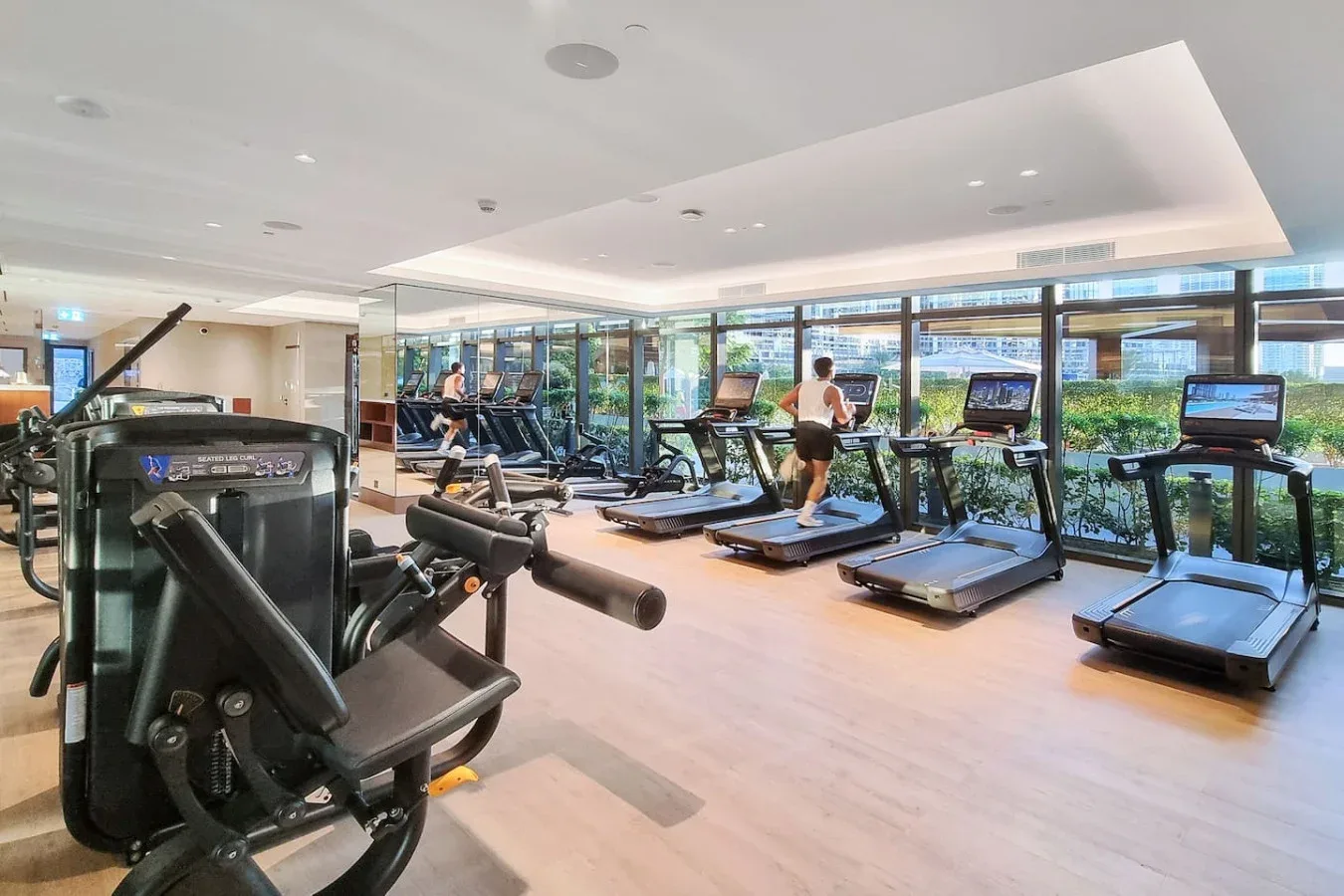 A gym with treadmills and other exercise equipment beside large windows.