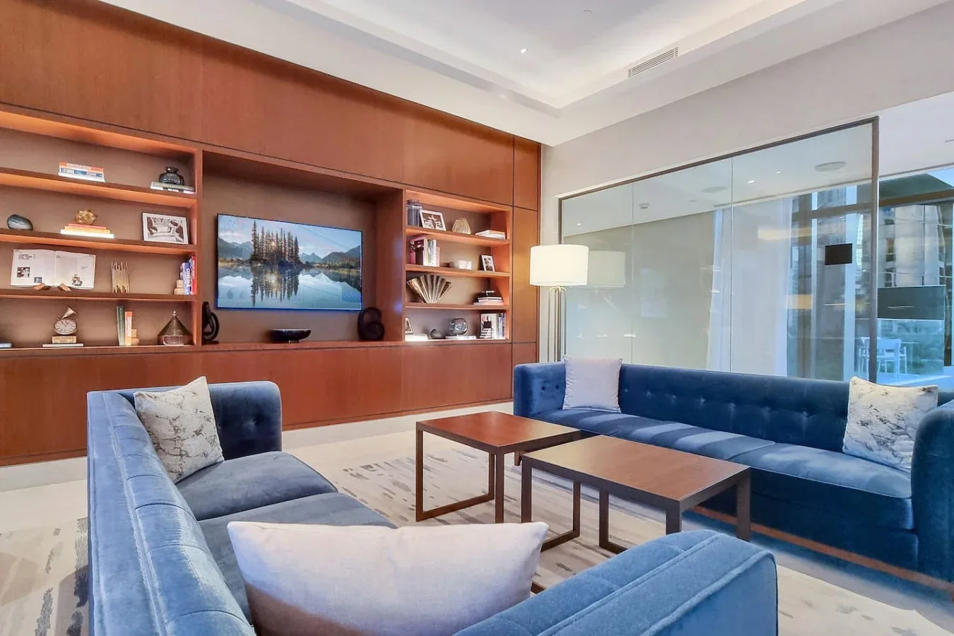 A lounge with blue seating, wooden tables, and built-in shelving.