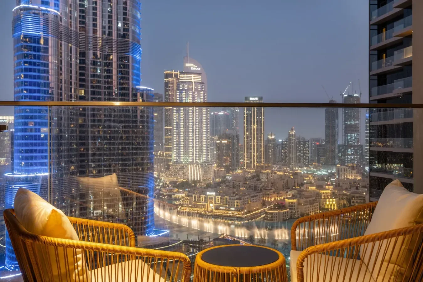 A balcony seating area overlooks a brightly lit city skyline at dusk.