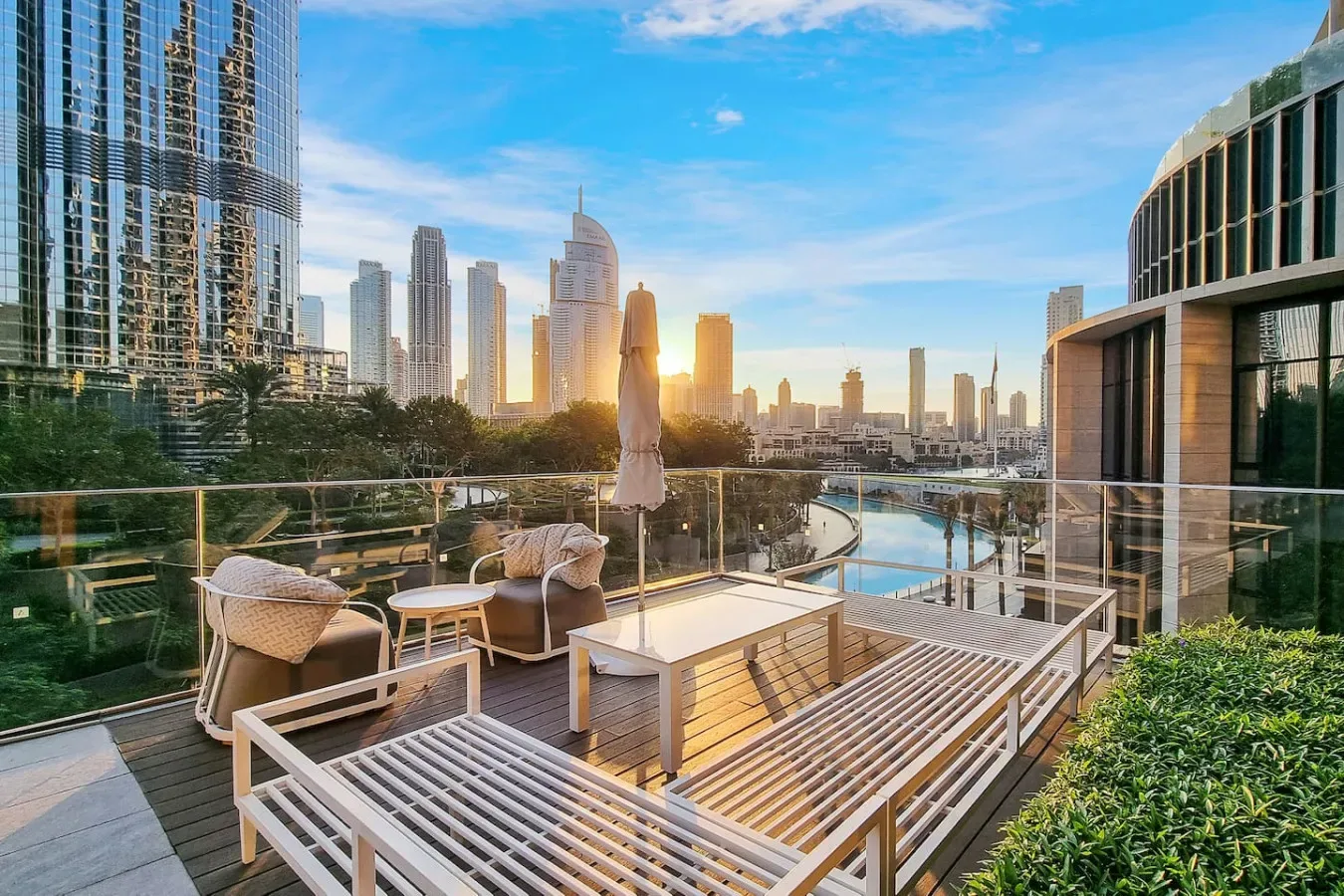 A rooftop terrace overlooks a city skyline at sunset, with outdoor seating beside a pool.
