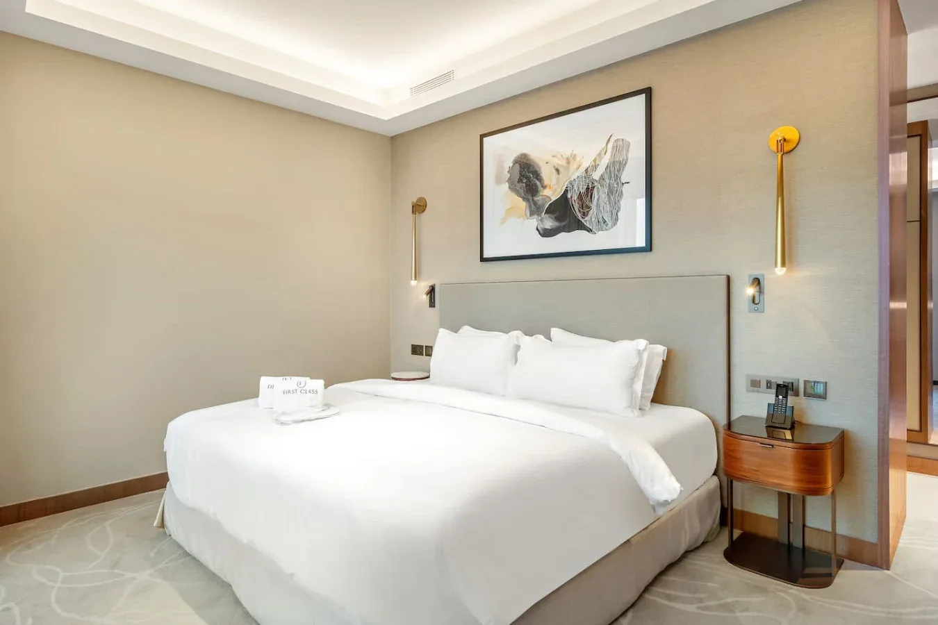 A bedroom with a large bed beneath framed artwork and wall lights.