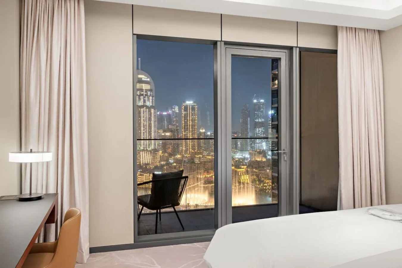 A bedroom with floor-to-ceiling windows overlooking a city skyline at night.