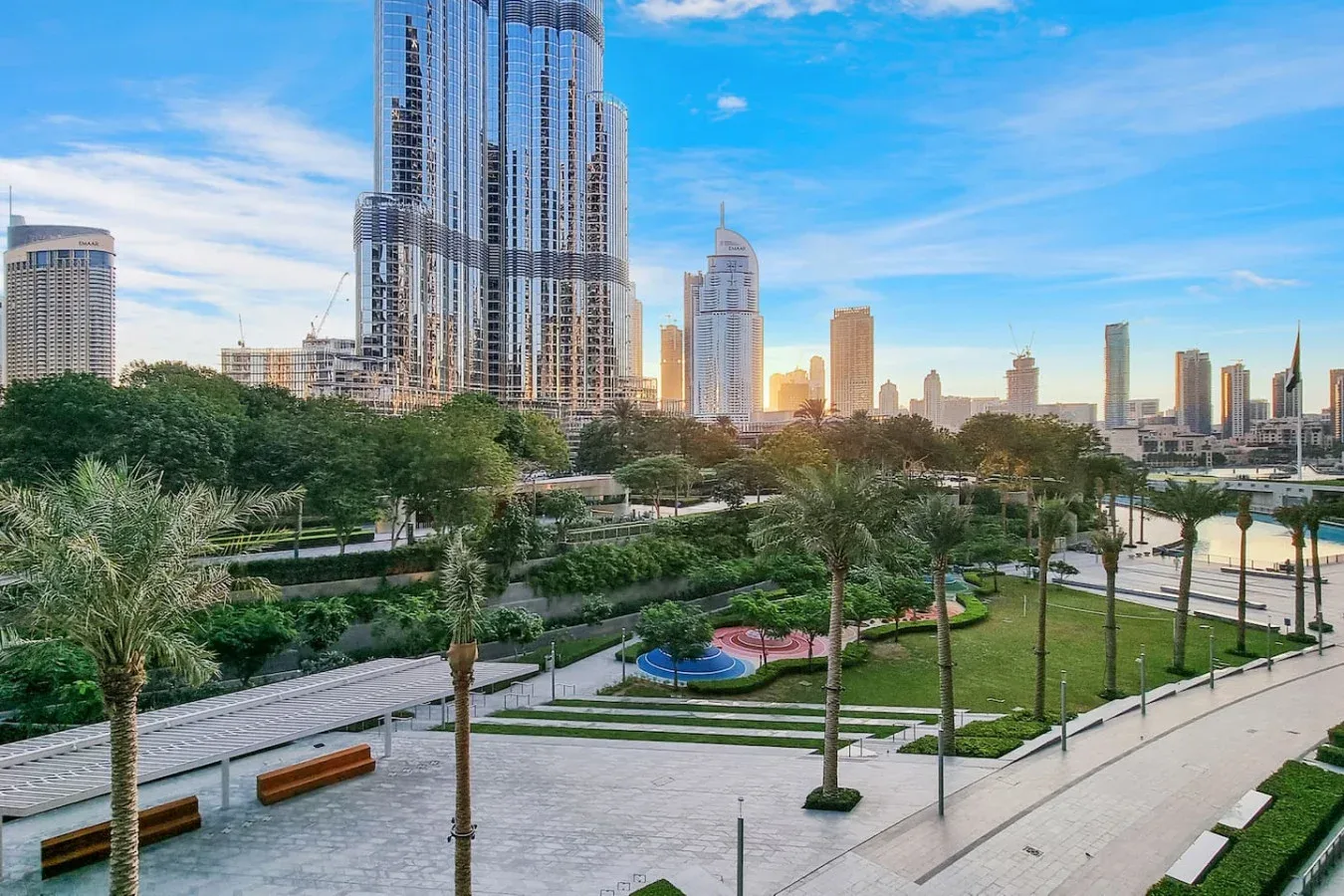 A landscaped urban park with paved paths and modern high-rise buildings in the background.