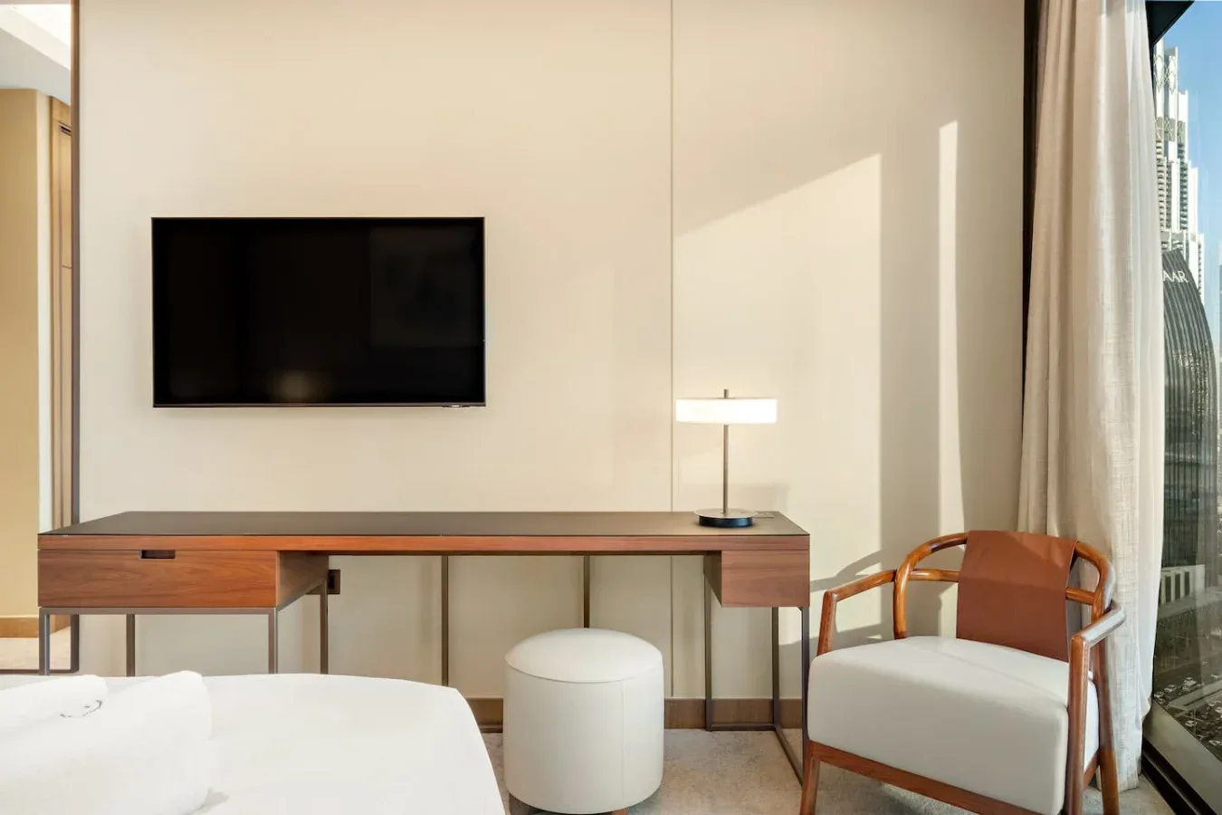 A bright bedroom seating area features a wall-mounted television and a desk.