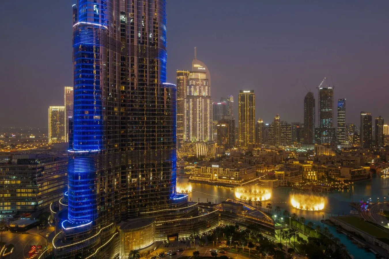A nighttime city skyline with illuminated skyscrapers beside a waterfront.