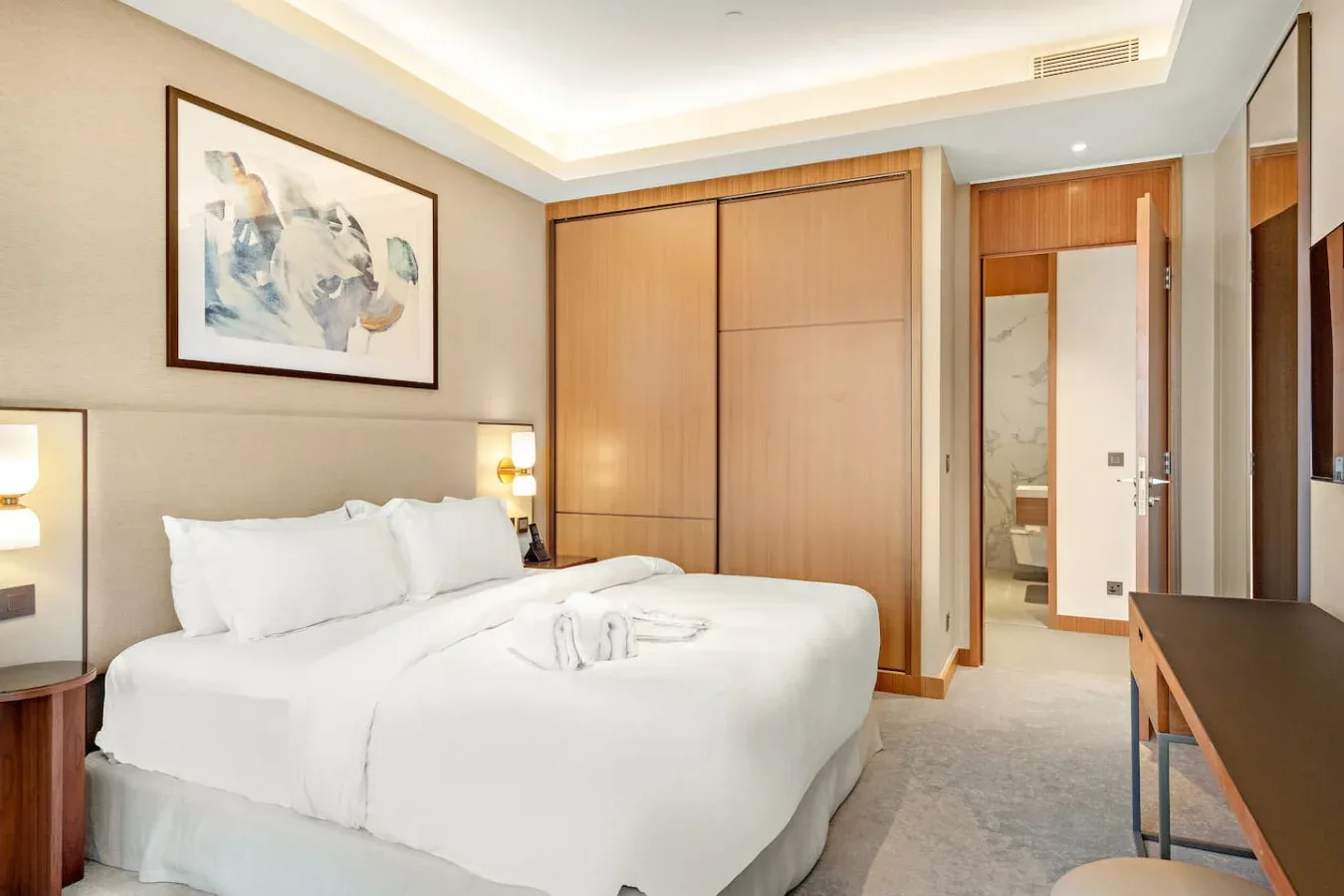A bedroom with a bed, framed artwork, and wooden wardrobe.