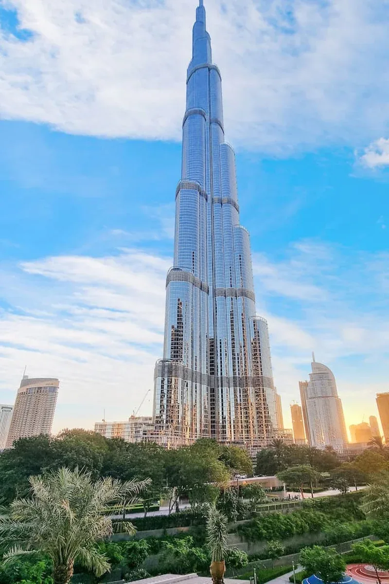The Burj Khalifa rises above landscaped greenery beneath a partly cloudy sky.