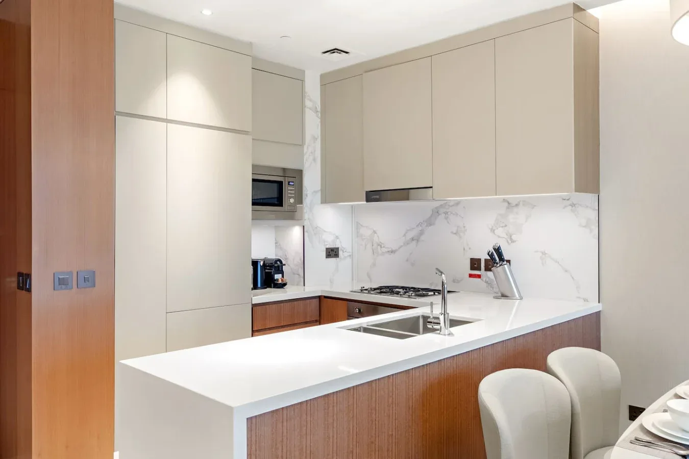 A modern kitchen with pale cabinets, a marble-patterned backsplash, and a bright island.