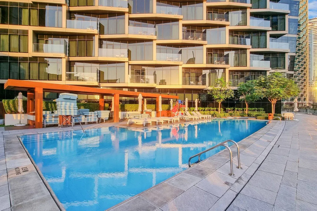 A swimming pool sits beside a modern building with balconies and outdoor seating.