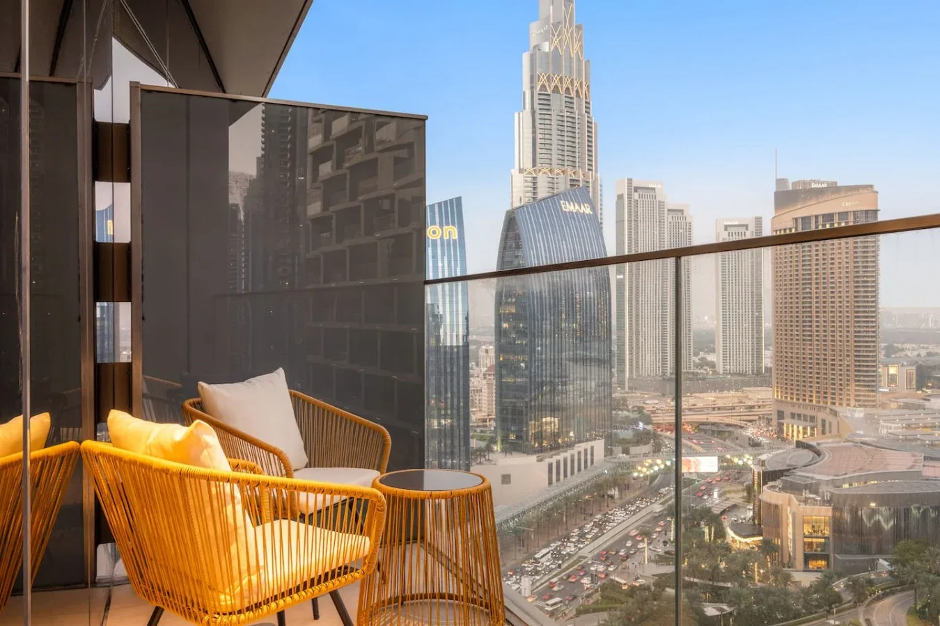 A balcony seating area overlooks a city skyline through a glass railing.