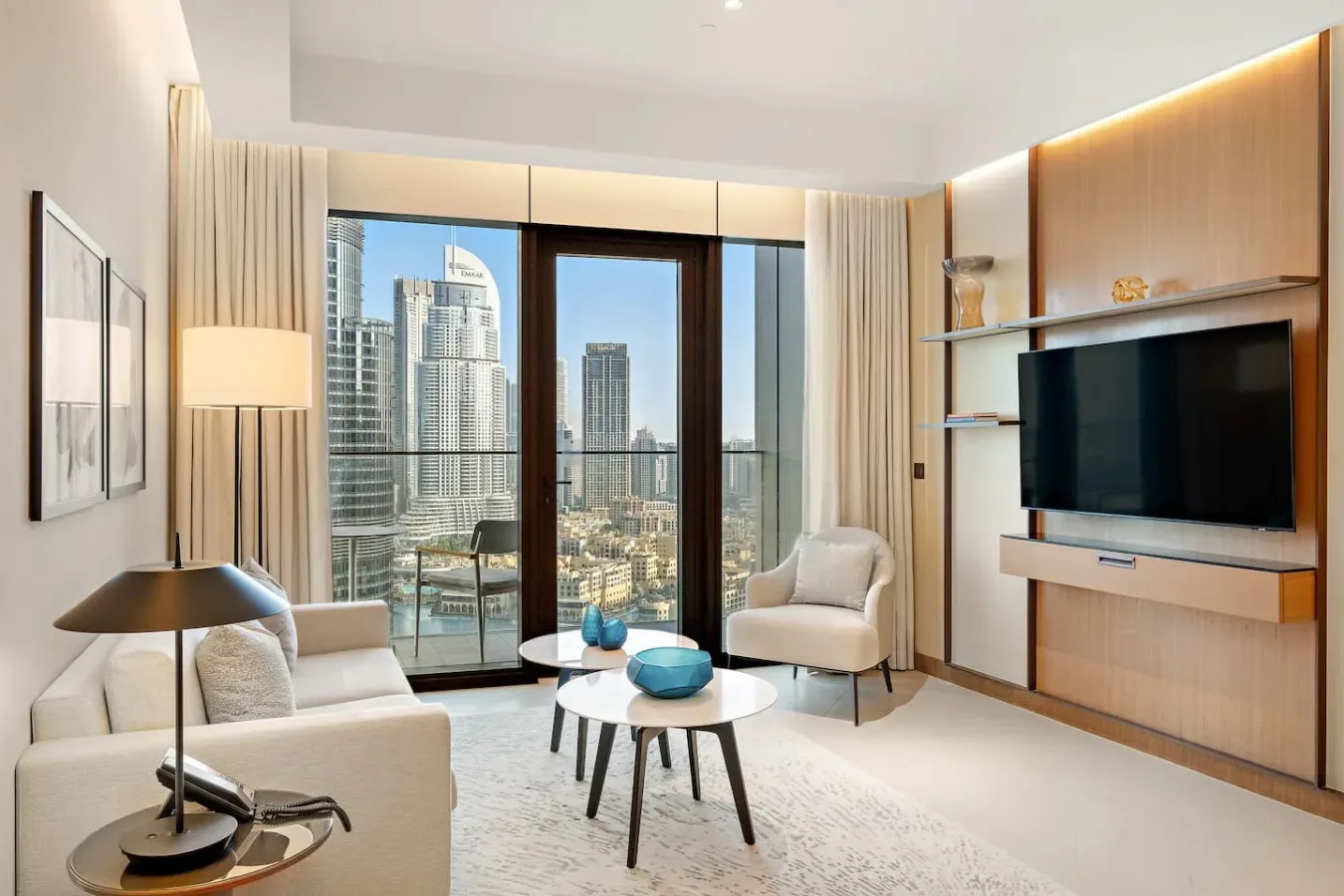 A modern living room with seating, a television, and large windows overlooking city buildings.