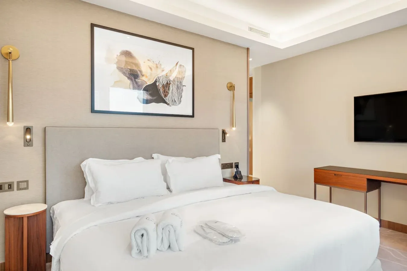 A bedroom with a neatly made bed, framed artwork, and a wall-mounted television.