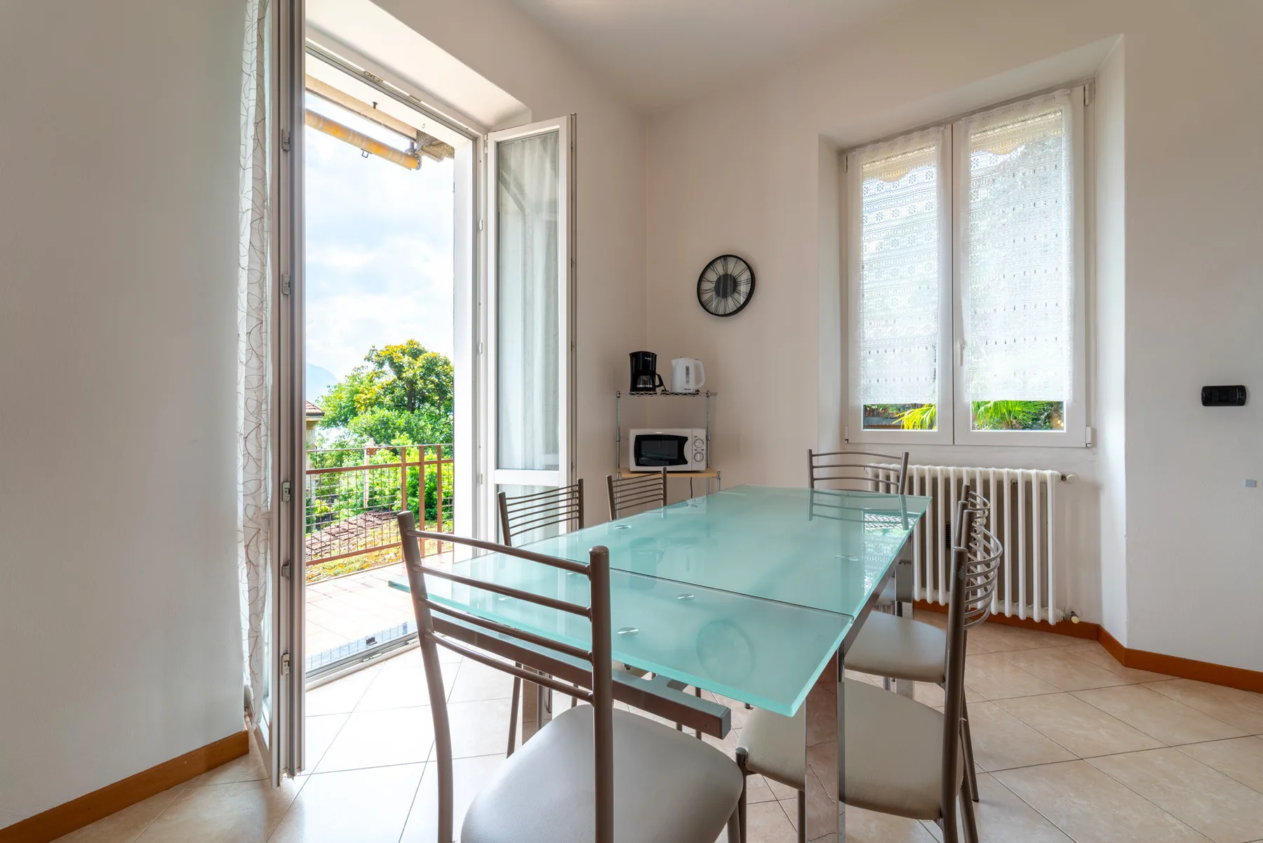 A dining area with a glass table and an open balcony door.