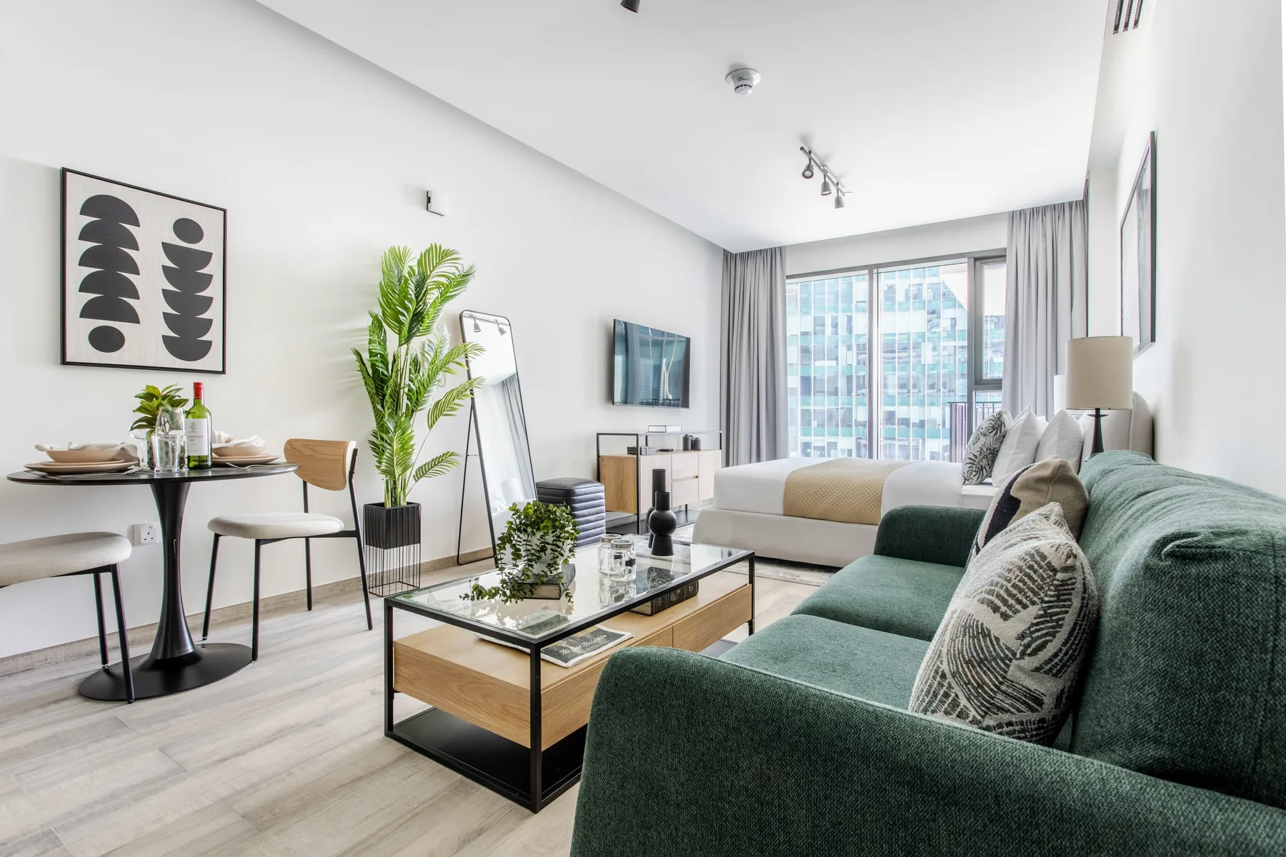 Una sala de estar luminosa con asientos verdes, una mesa de centro y ventanas grandes.