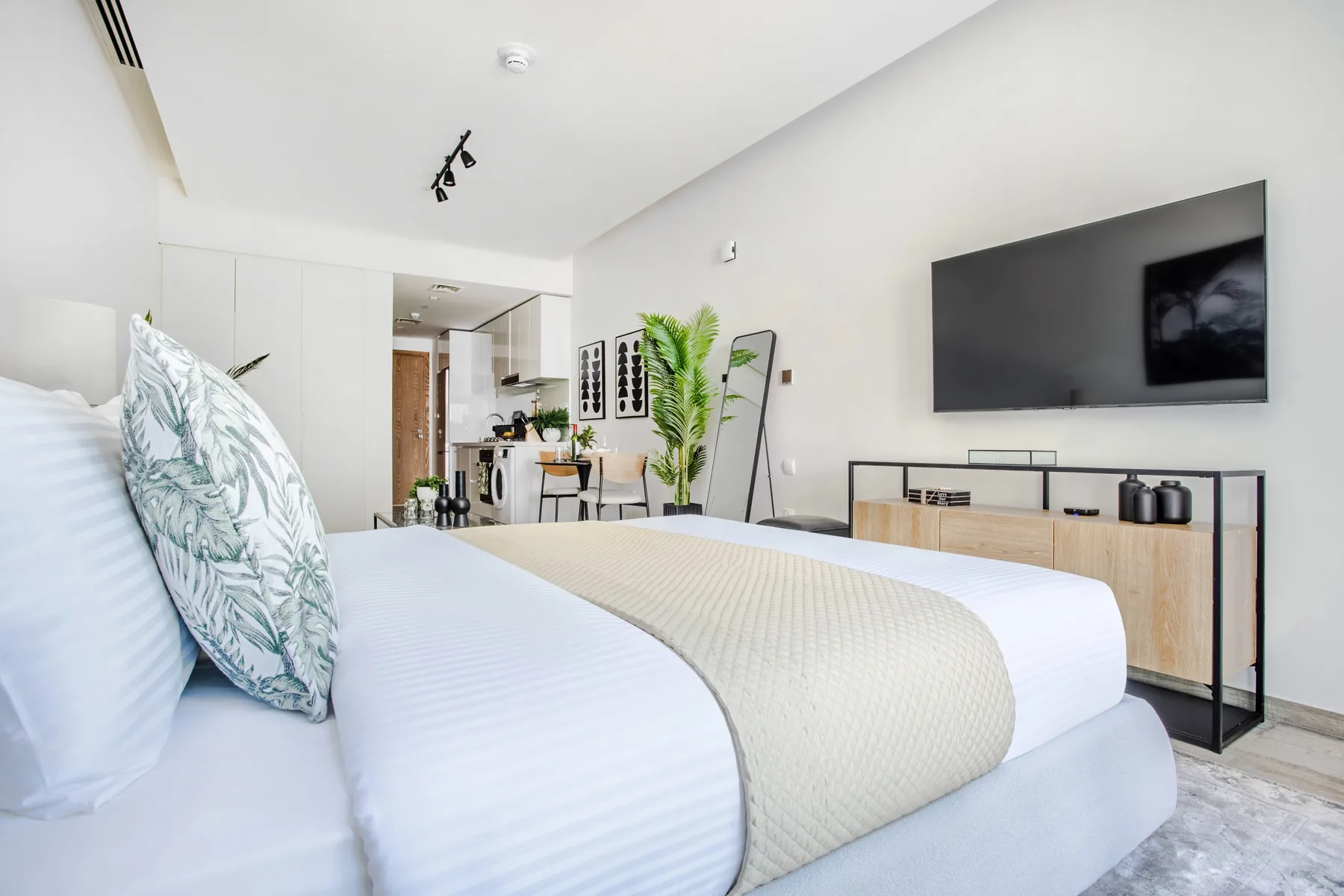 Un dormitorio luminoso cuenta con una cama bien hecha y un televisor montado en la pared.