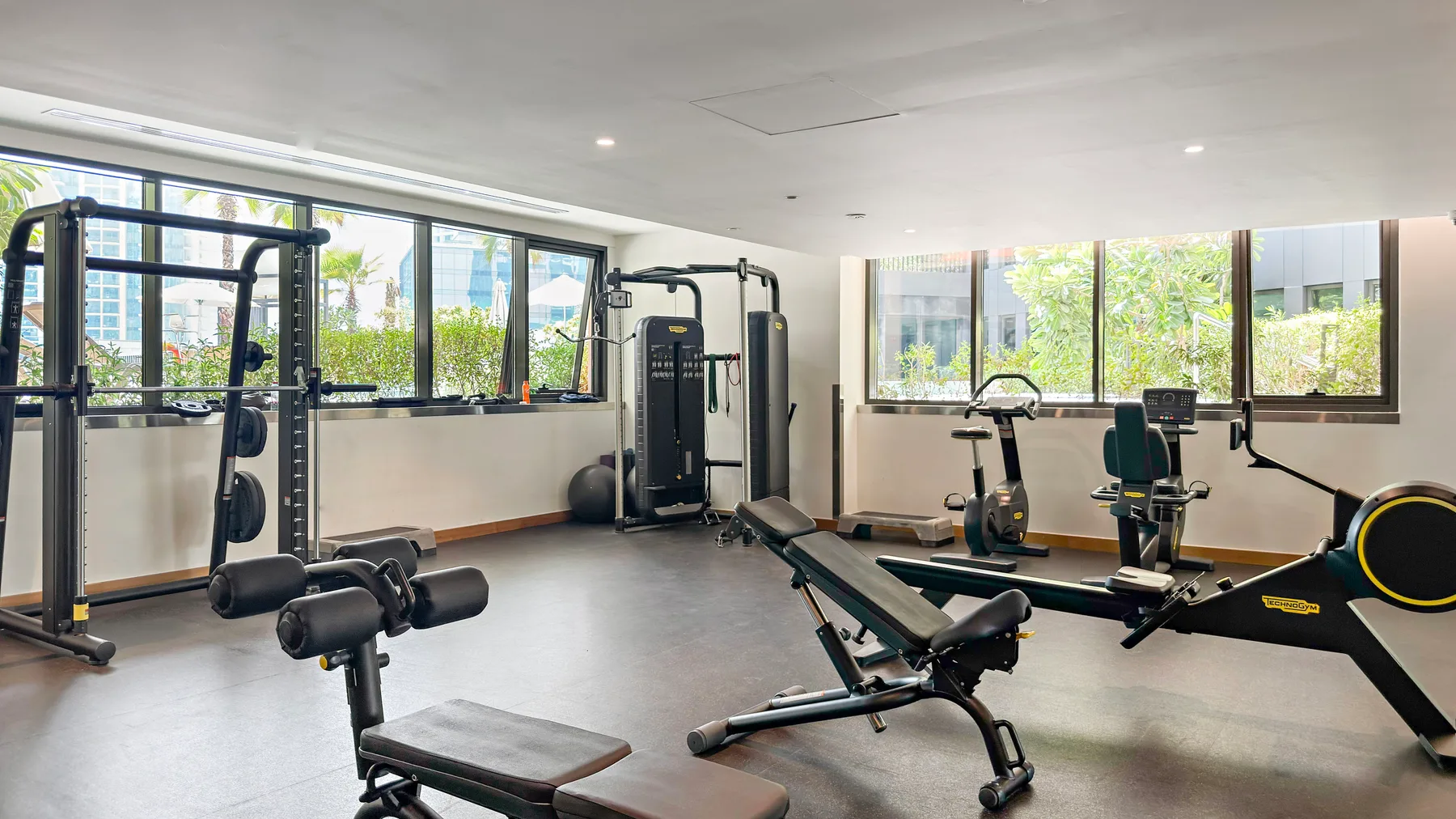 Una sala de ejercicio luminosa con máquinas y grandes ventanas.