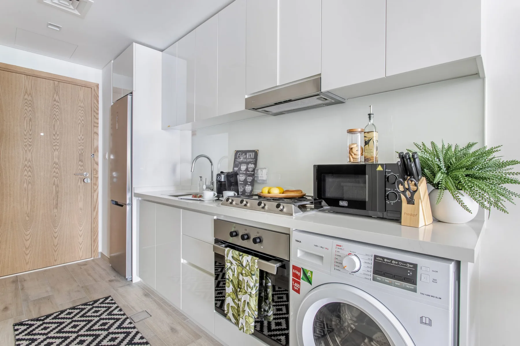 Una cocina compacta con armarios blancos, placa de cocina, microondas y lavadora.