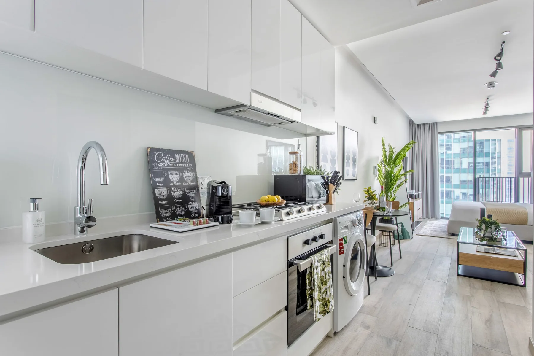 Una luminosa cocina abierta al salón, con muebles blancos y grandes ventanas.