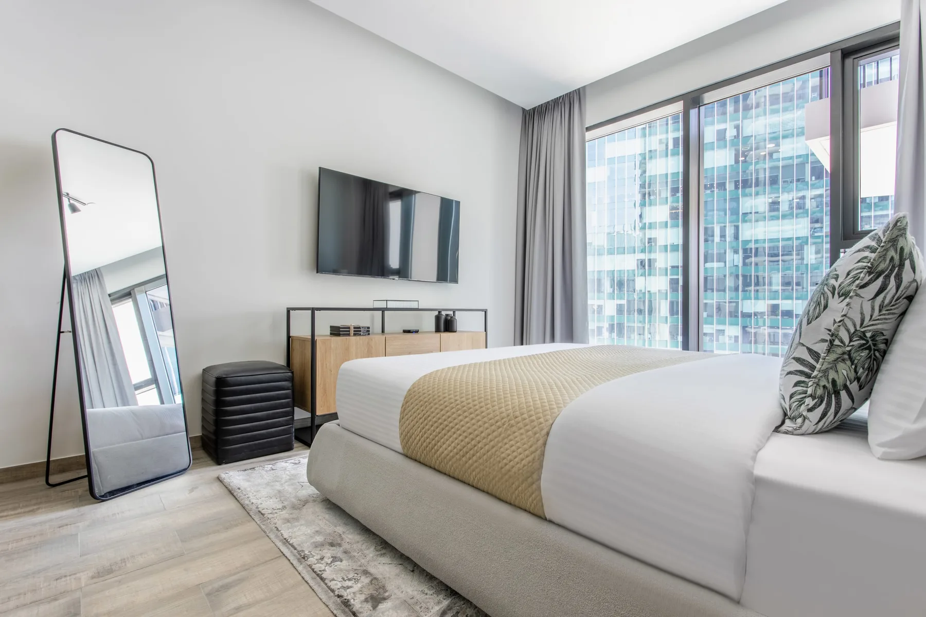 Un dormitorio luminoso con una cama tendida junto a ventanas de piso a techo.