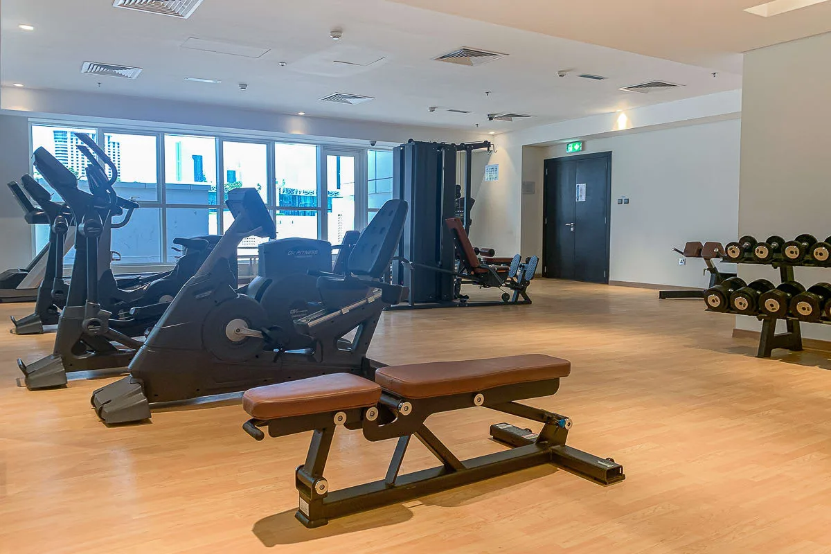 Un gimnasio con máquinas de ejercicio, bancos y un soporte para pesas.