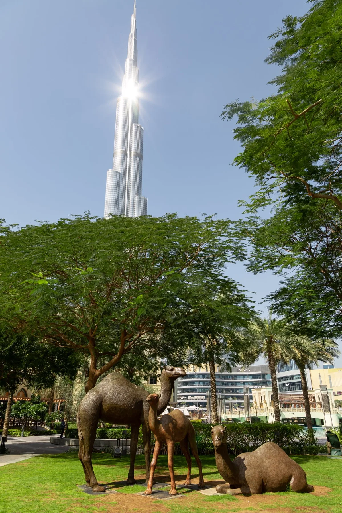 Un espacio ajardinado al aire libre con esculturas de camellos bajo el Burj Khalifa.
