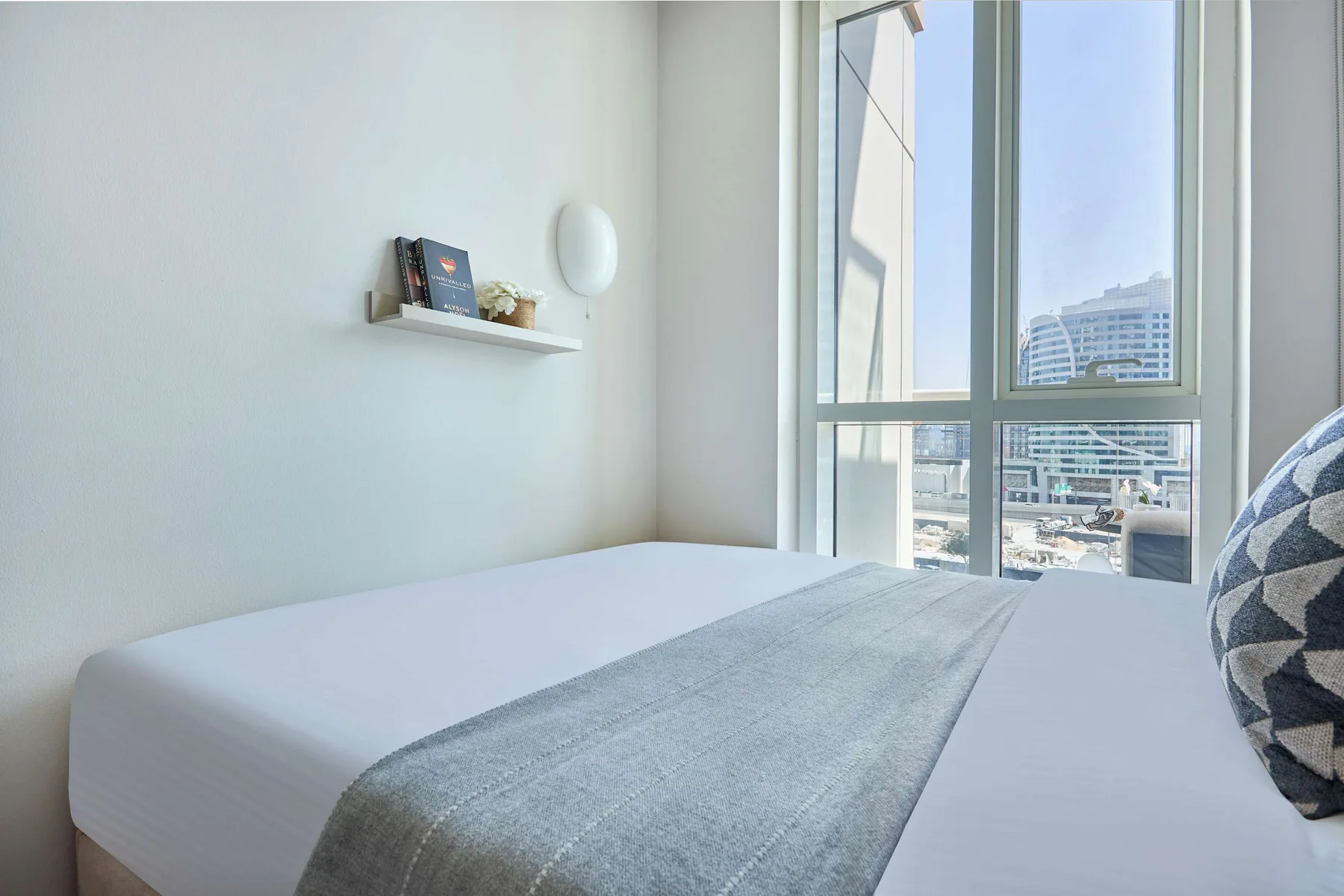 Un dormitorio luminoso con una cama bien hecha junto a una ventana grande.