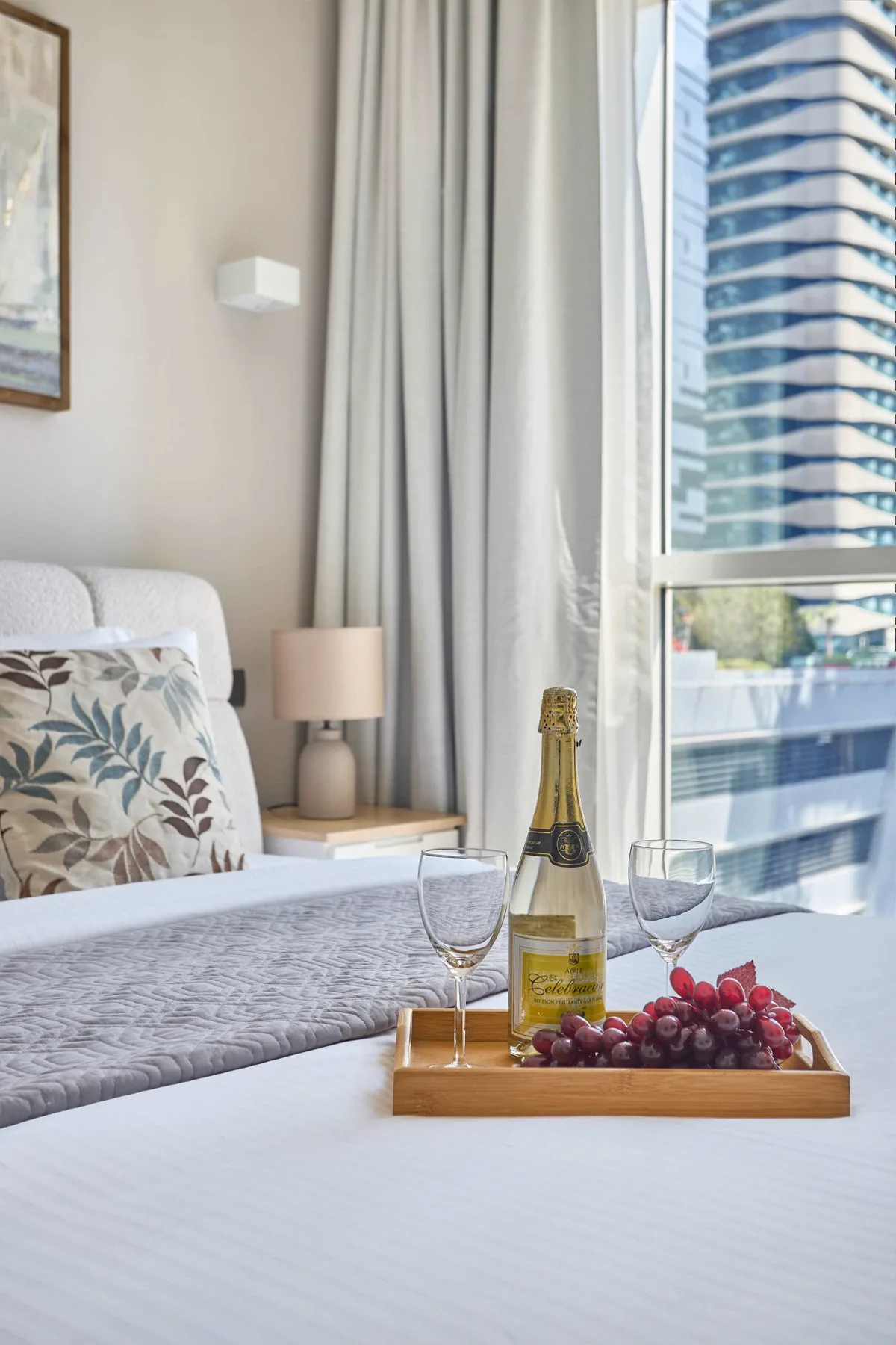 Un dormitorio luminoso con una cama, una mesita de noche y una bandeja con fruta y vino espumoso.