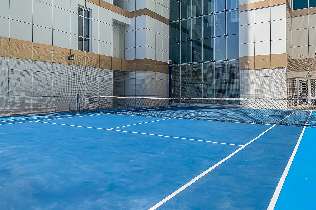 Una cancha deportiva azul al aire libre con líneas blancas junto a un edificio moderno.