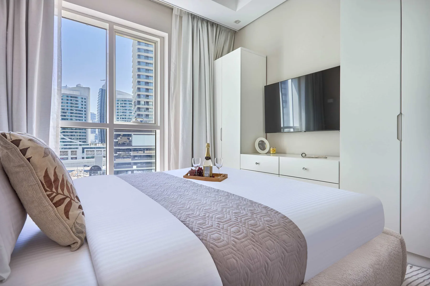 Un dormitorio luminoso con una cama arreglada y una gran ventana con edificios a la vista.