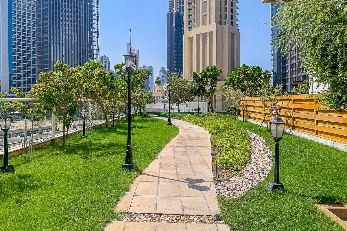 Un patio ajardinado con un sendero pavimentado, césped verde y edificios altos alrededor.