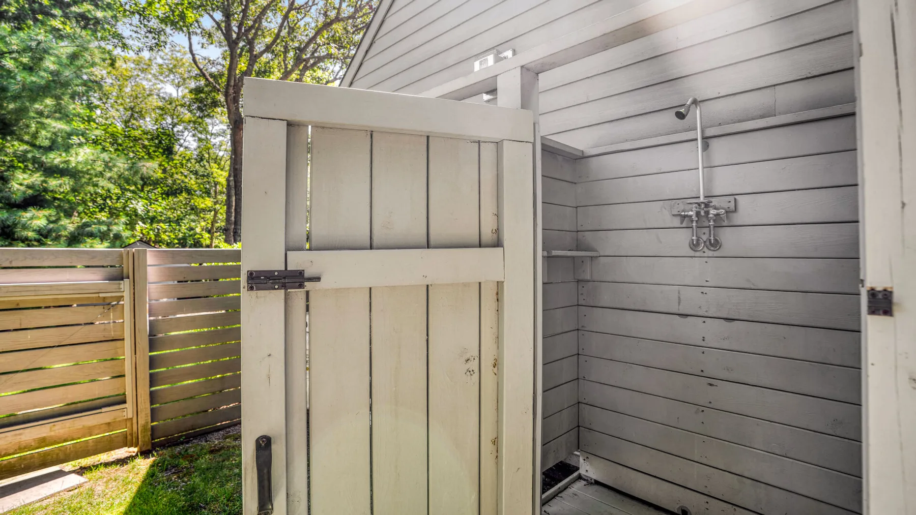 Una zona de ducha exterior con una pantalla de madera y árboles alrededor.