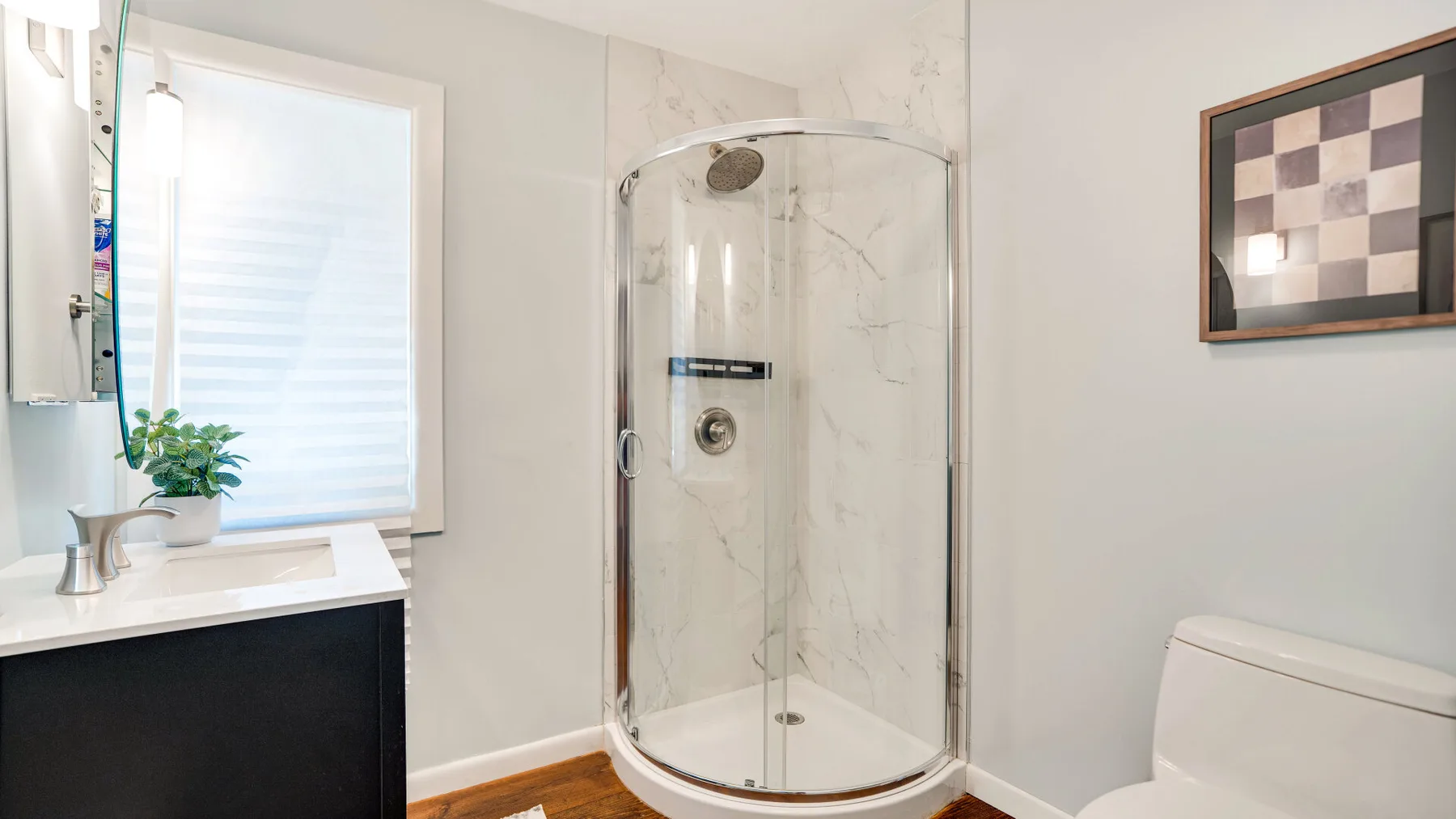 Un baño luminoso con una ducha de vidrio curvada y un lavabo.