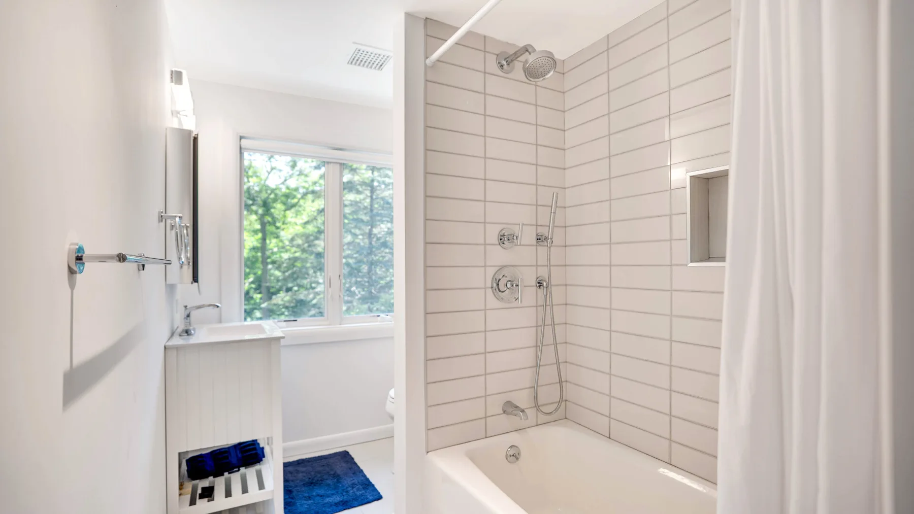 Un baño luminoso con ducha de azulejos y una ventana con vistas a la vegetación.