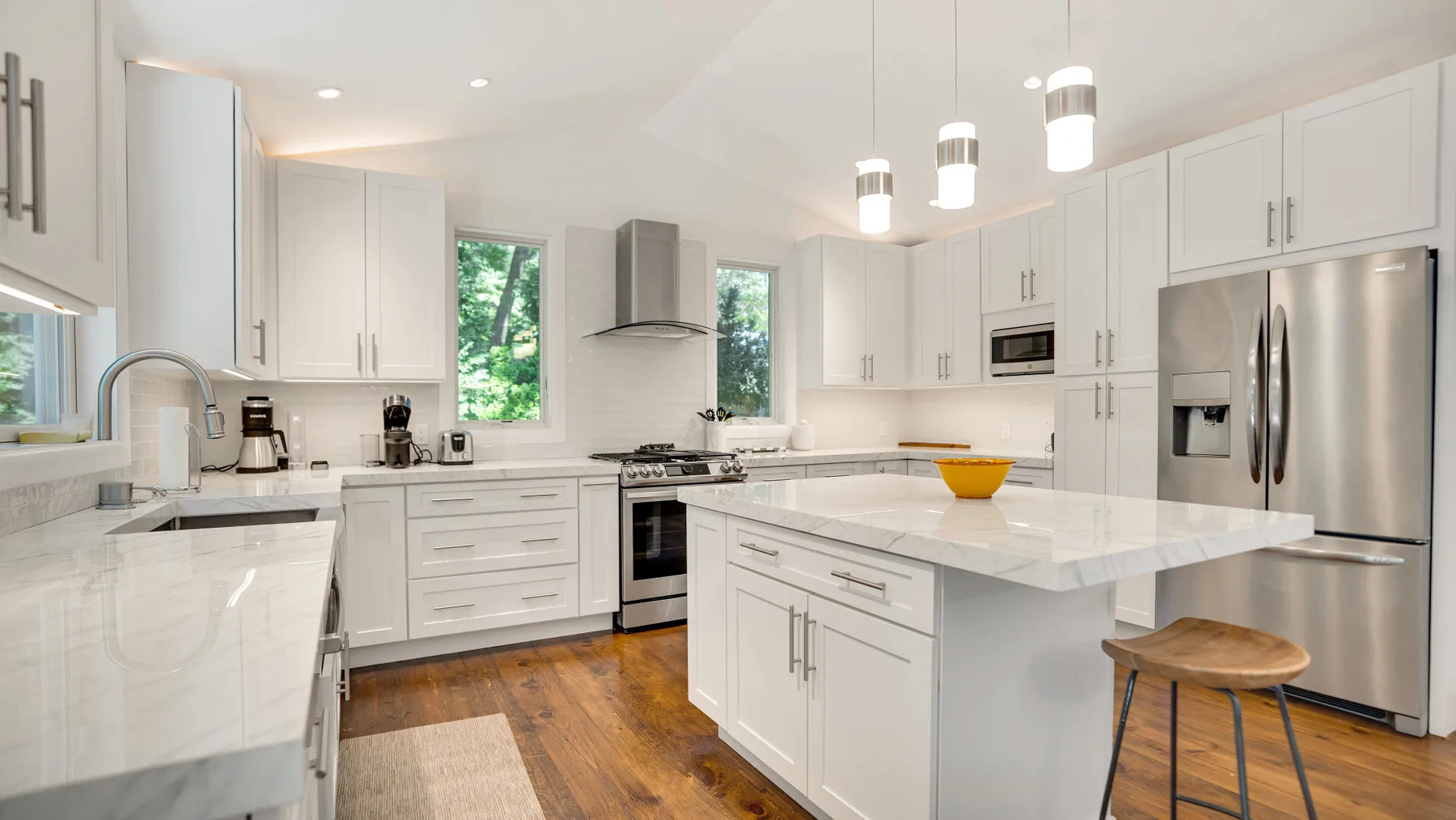 Una cocina luminosa con gabinetes blancos, una isla central y electrodomésticos de acero inoxidable.