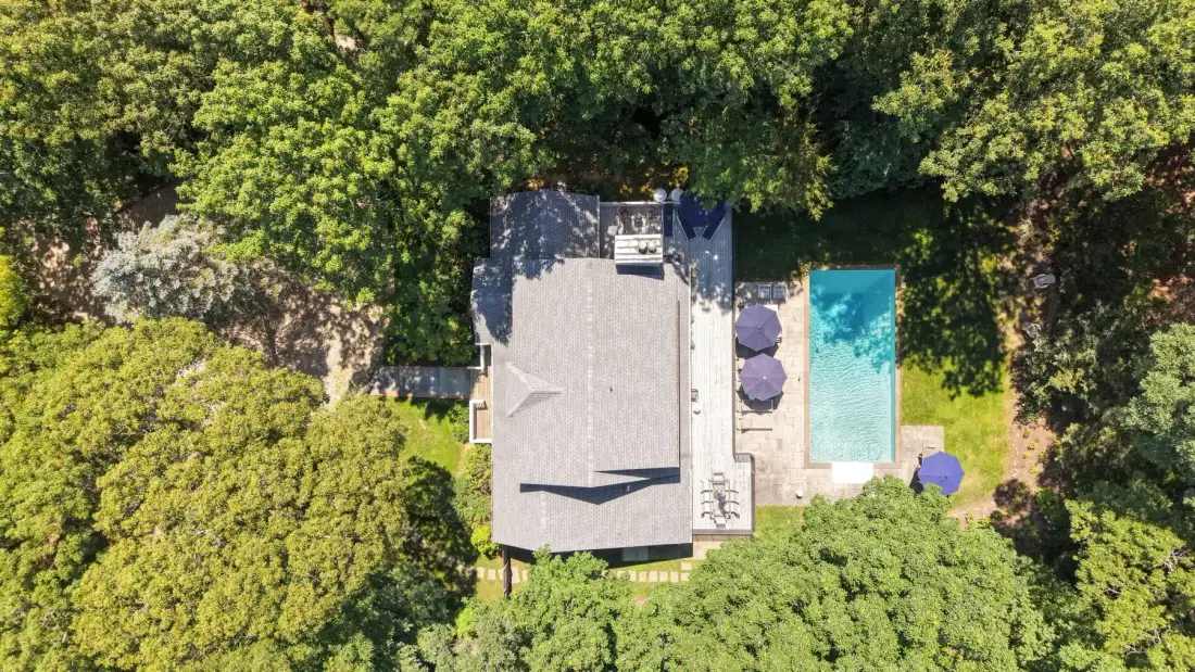 Vista aérea de una casa y una piscina rodeadas de árboles.