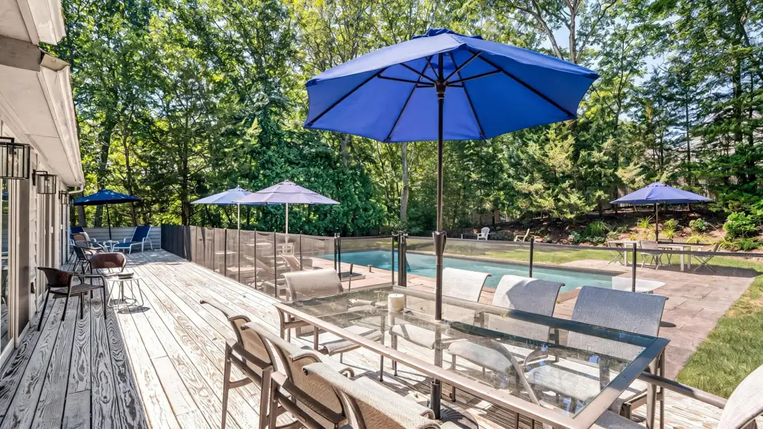 Un patio junto a una piscina con asientos bajo una sombrilla azul.