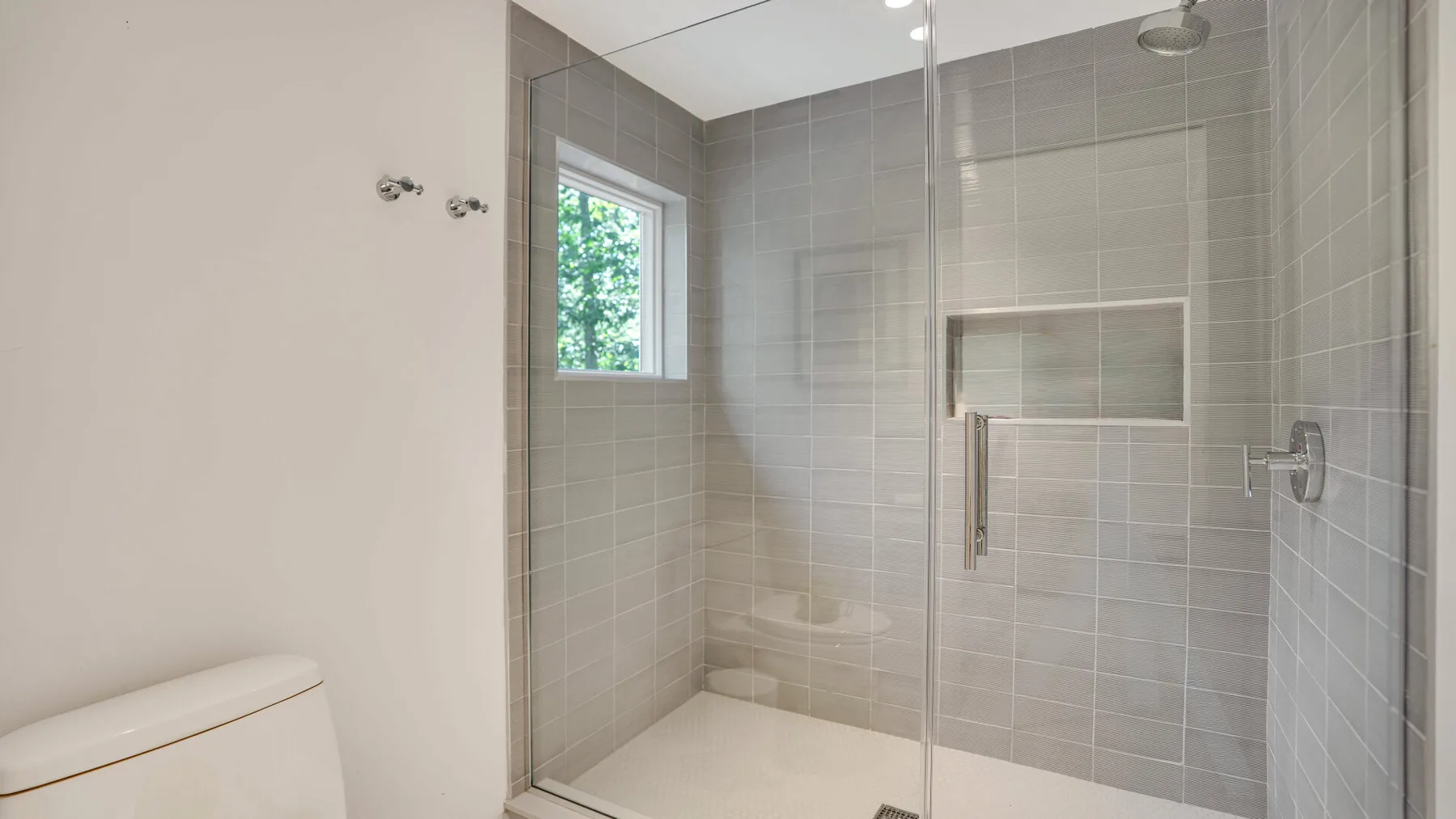 Un baño alicatado con ducha de cristal y una ventana.