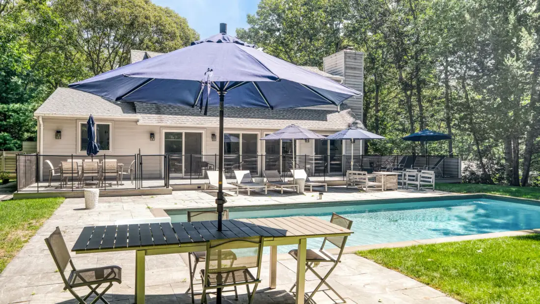 Un patio trasero da a una piscina, con asientos al aire libre junto a la casa.