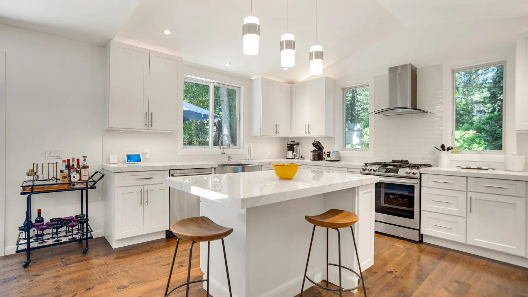 Una cocina luminosa con gabinetes blancos, una isla central y ventanas grandes.