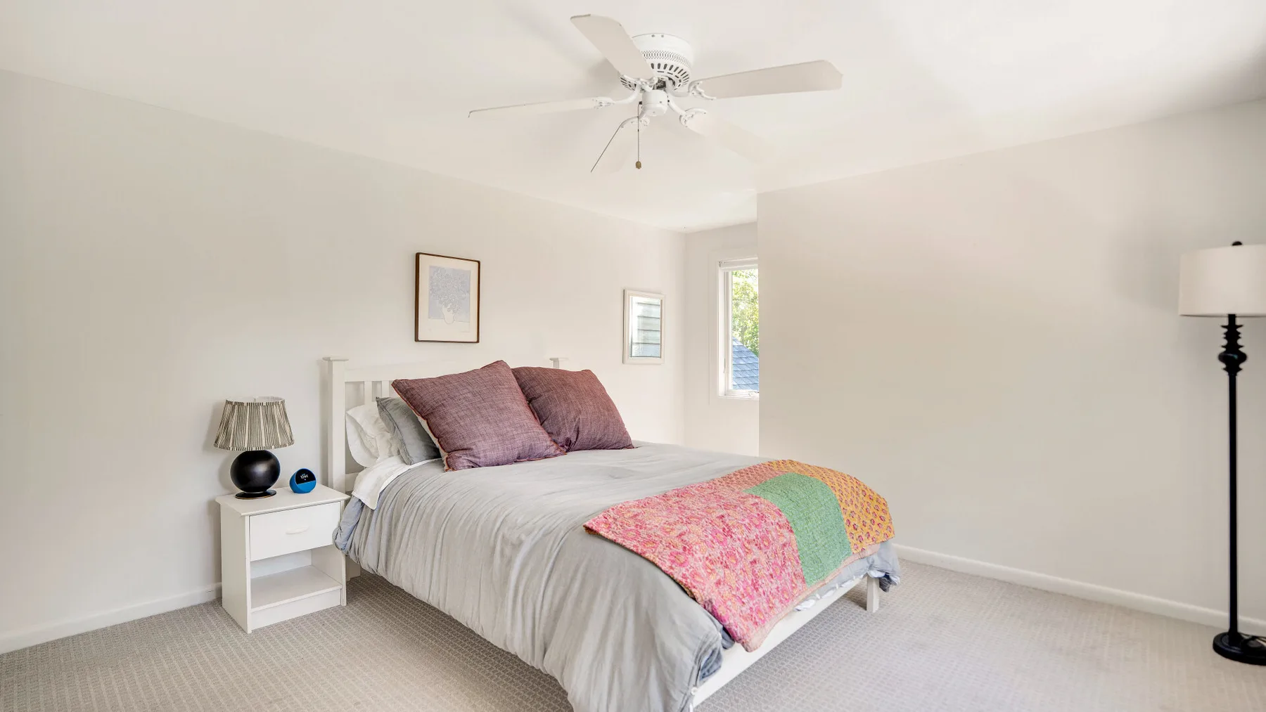 Un dormitorio luminoso con una cama, una mesita de noche y un ventilador de techo.
