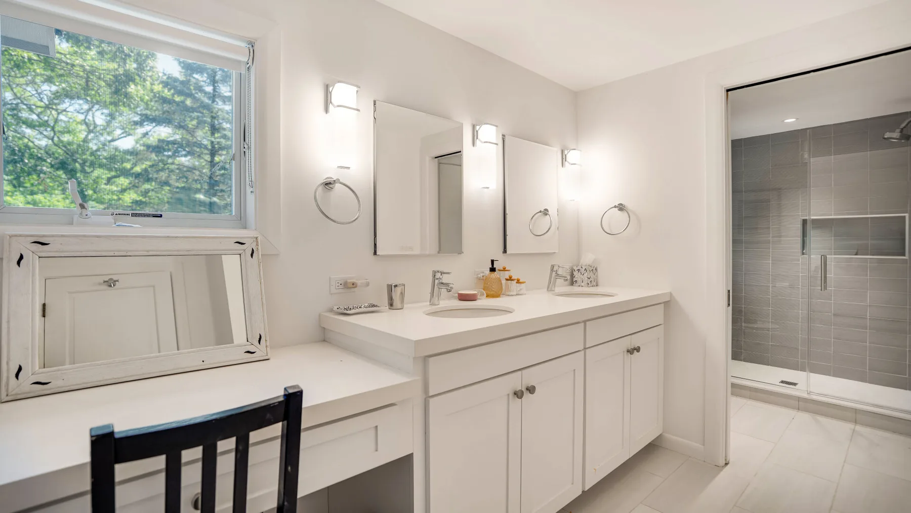 Un tocador de baño luminoso con espejos y una ventana con vistas a los árboles.