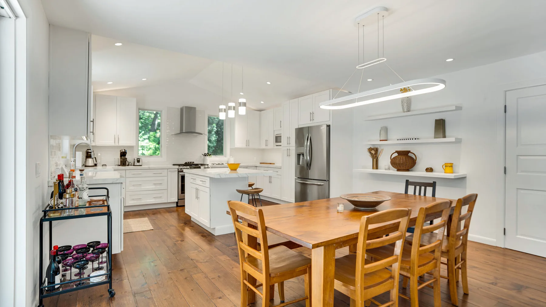 Una cocina y comedor de concepto abierto, luminosos, con gabinetes blancos y una mesa de madera.