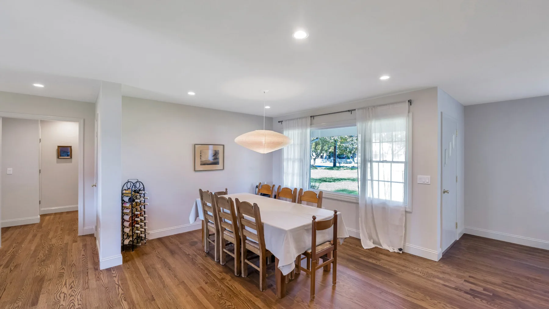 A dining area with a long table beside large windows.