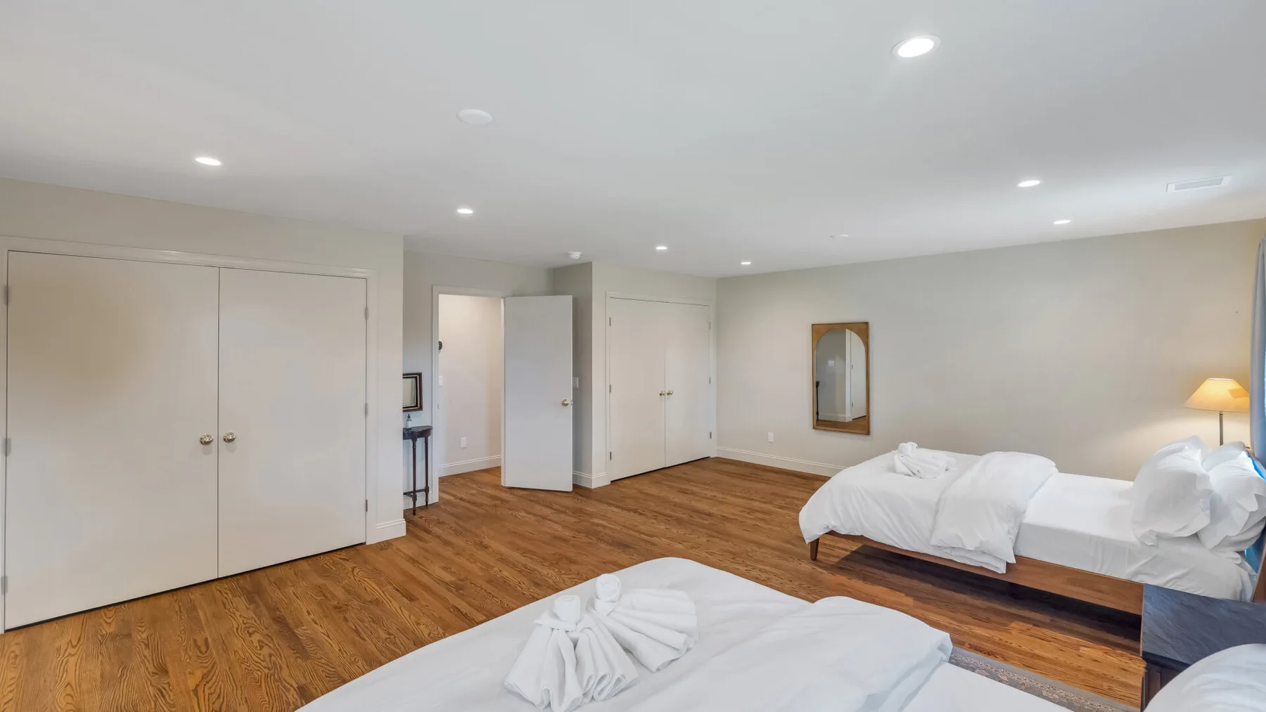 A bedroom with beds, wood flooring, and a mirrored wall.