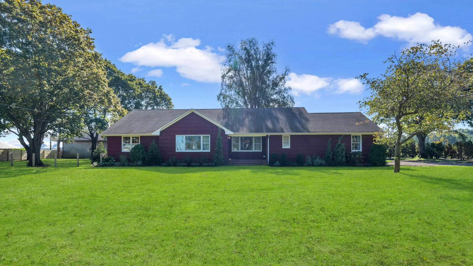 A single-story red house stands beyond a broad green lawn.