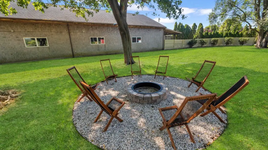 A grassy outdoor yard has a circular gravel seating area around a fire pit.