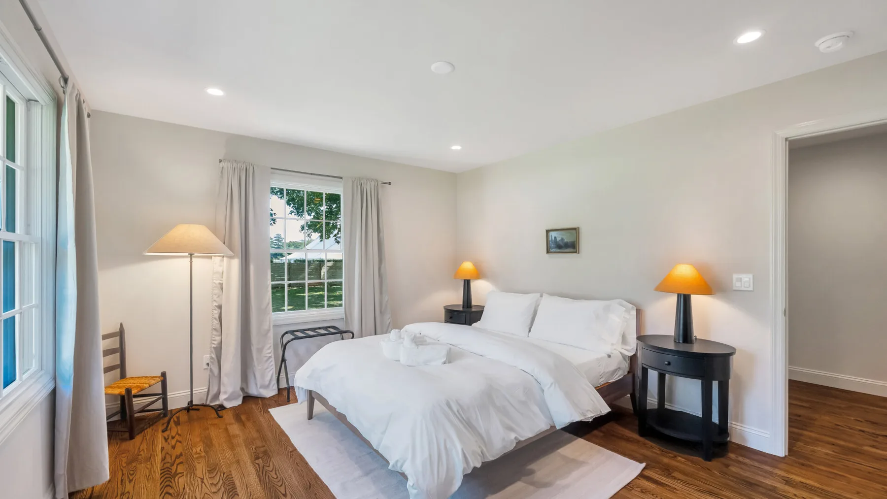 A bright bedroom with a bed, bedside tables, and a window with curtains.