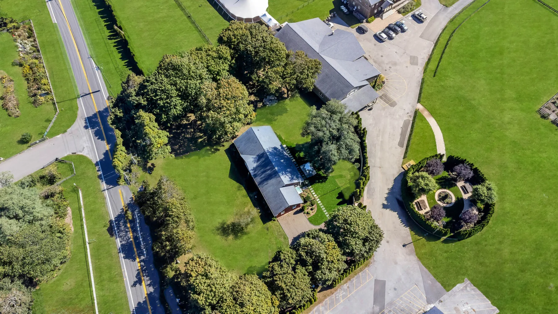 Aerial view of a landscaped property with buildings, trees, and a circular garden.