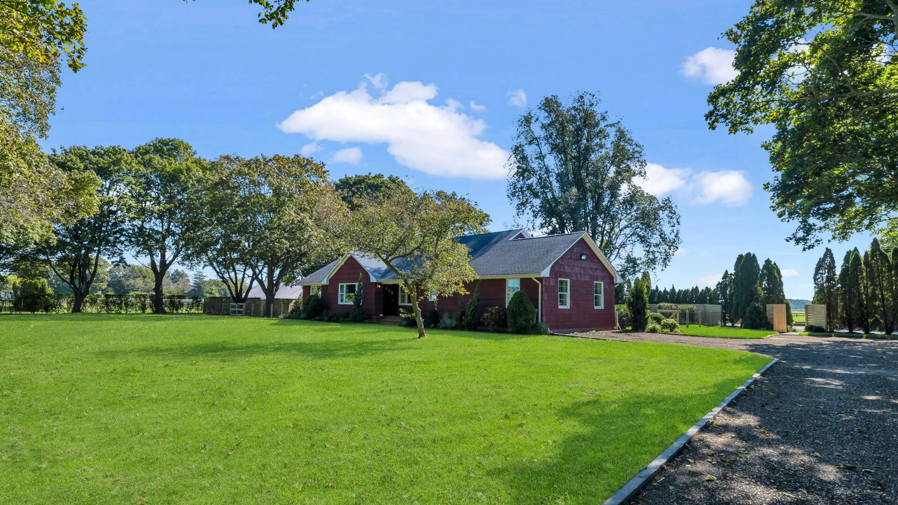 A red house stands beside a broad green lawn and gravel driveway.